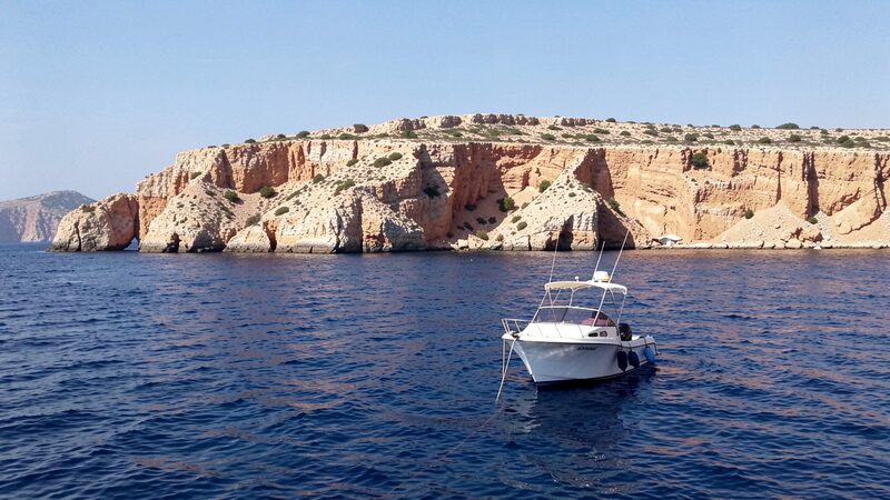 Islote rocoso mediterraneo visto desde el mar con acantilados ocres y agua azul profunda en primer plano